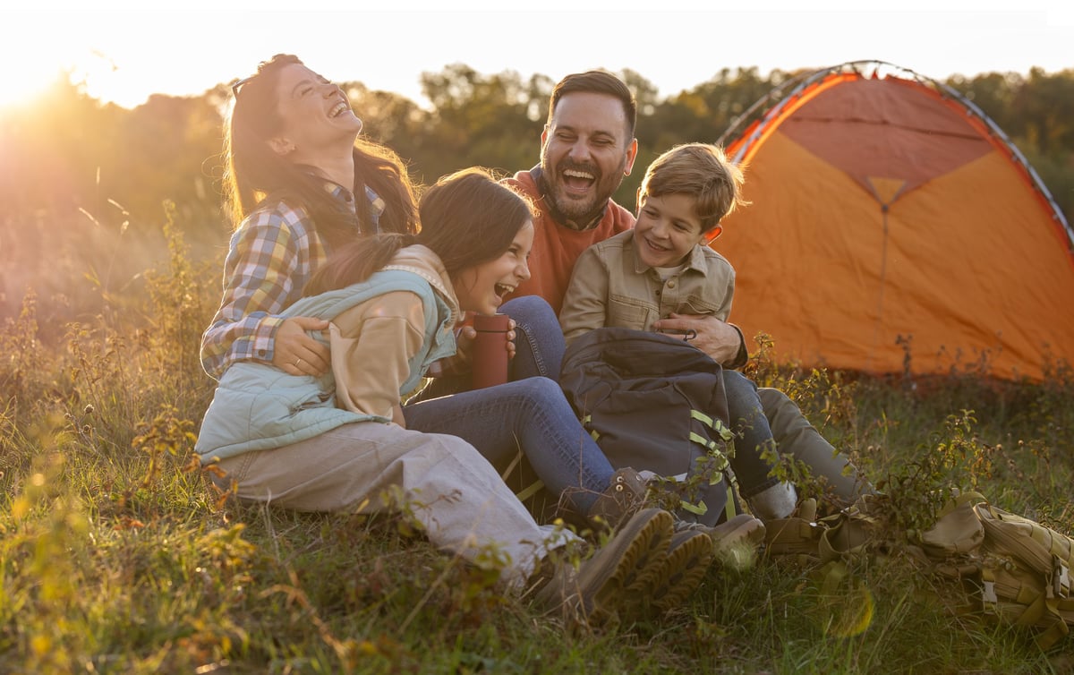 Familia riendo junto a su casa de campaña al atardecer, bajo el cielo de Baja California Sur