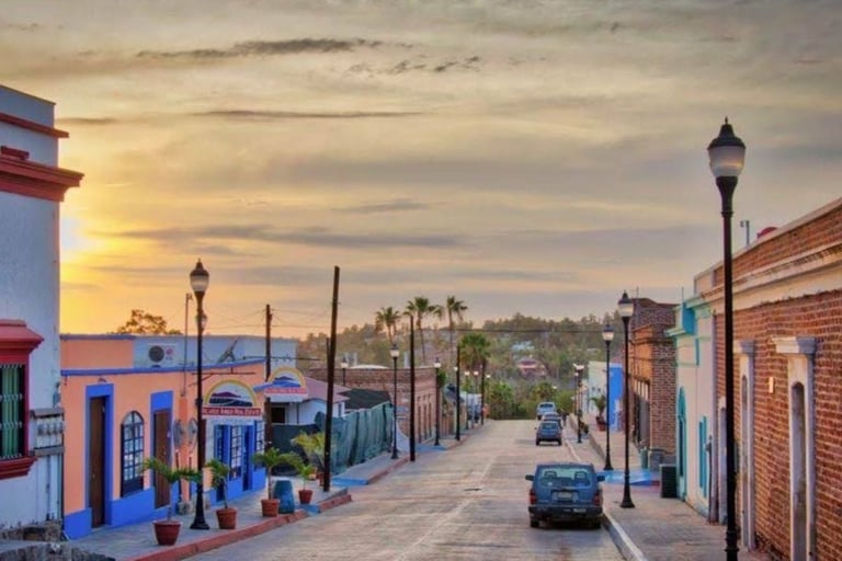 Colorful street in historic downtown district at sunset with brick buildings, street lamps, parked car, and palm trees in background