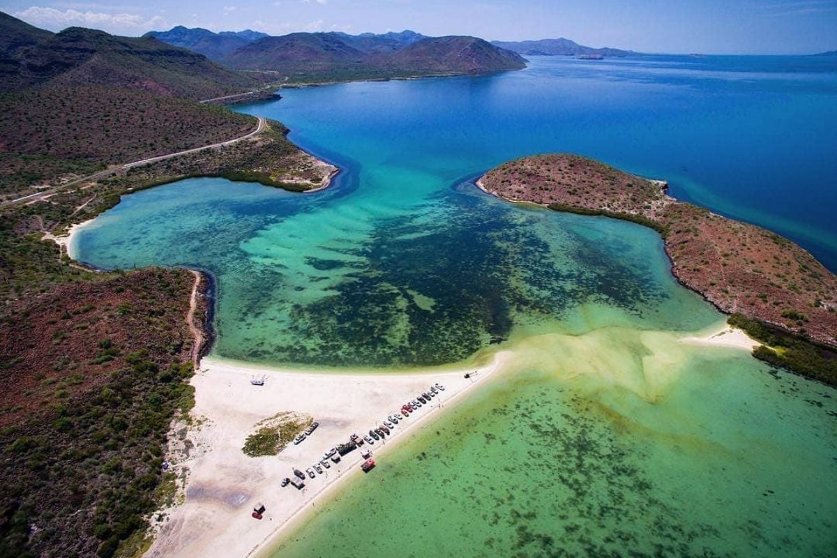 Aerial view of a tropical island with turquoise waters, white sandy beach, and sparse vegetation surrounded by blue sea