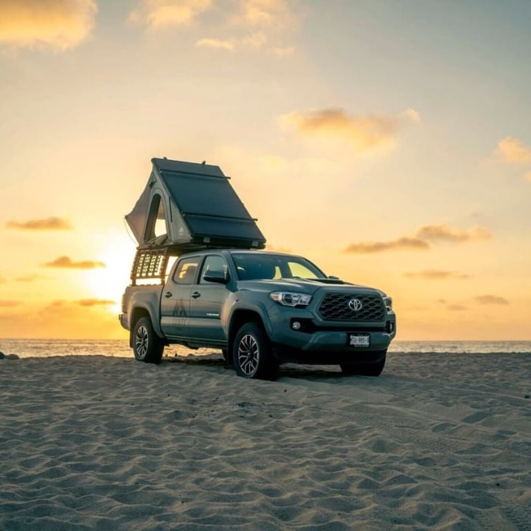 Blue Toyota truck with pop-up camper roof parked on sandy beach at sunset