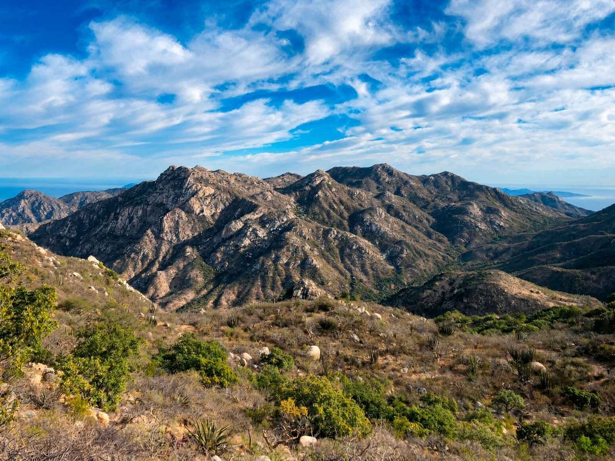 Montañas rocosas con vegetación dispersa del sendero El Puerto bajo cielo azul con nubes blancas