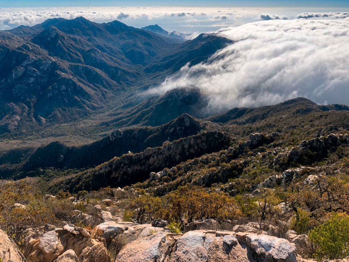 Paisaje de montaña del sendero El Puerto con picos, laderas y niebla en el valle bajo cielo despejado