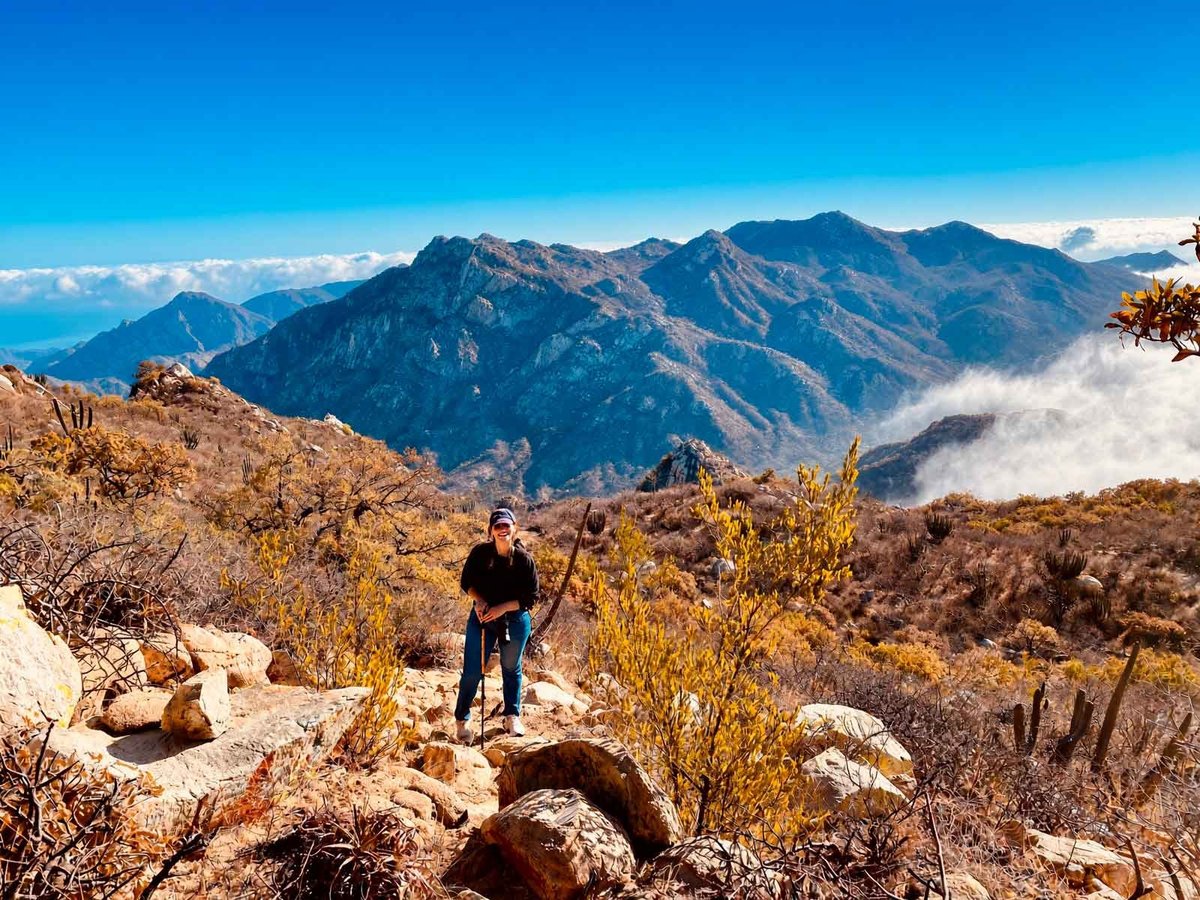 Sendero El Puerto, La Paz — excursionista de pie en ladera rocosa mirando cordillera con cielo azul