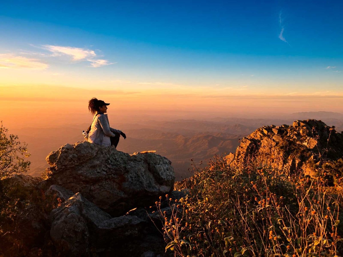 Sierra La Laguna trek, person standing on a rocky peak above canyons at sunset